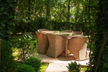 Hasır sandalyeler ve masa ağaçların yanındaki bahçede..