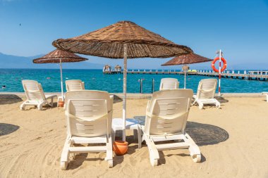 Kumsala beyaz plaj güneşlikleri ve şemsiyeler konmuştu. Arkadaki mavi gökyüzü ve dağ. Tatil ve tatil plaj konsepti.
