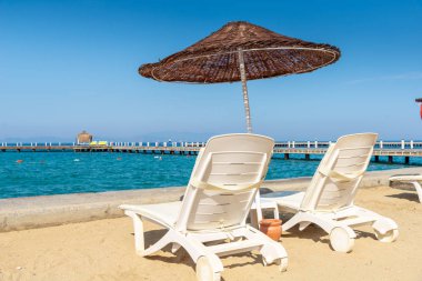 Kumsala beyaz plaj güneşlikleri ve şemsiyeler konmuştu. Arkadaki mavi gökyüzü ve dağ. Tatil ve tatil plaj konsepti.