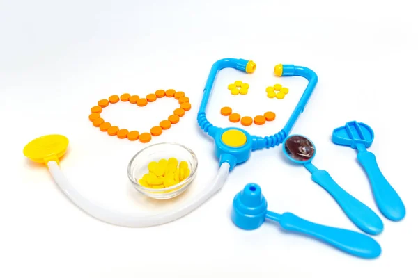 Blue stethoscope, otoscope, hammer, dental mirror Isolated on white background. Medicine concept. Childrens toys by profession doctor. A heart is by orange pills. Stethoscope smiles.