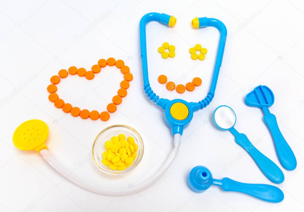 Medicine concept. Childrens toys by doctor. A heart is by orange pills.