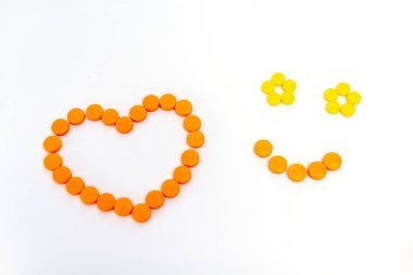 Bir kalp ve gülümseme turuncu hapları beyaz arka plan üzerinde izole vardır. Tıp kavramı.