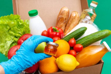 Yiyecek stoklarıyla dolu büyük bir kutu yeşillik karantina dönemi için gıda stoku. Sebze, yağ, şifalı bitkiler, izole edilmiş ekmek. Karantina, yemek teslimatı, bağış. Eldivenli bir el balı tutar..