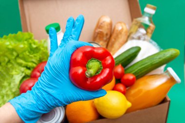 Yiyecek stoklarıyla dolu büyük bir kutu yeşillik karantina dönemi için gıda stoku. Sebze, yağ, şifalı bitkiler, izole edilmiş ekmek. Karantina, yemek teslimatı, bağış. Eldiven içinde dolmalık biber var..