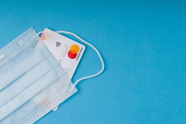 Kant, Kırgızistan - 31 Mart 2020: Mavi Medikal maske, mavi arka planda kredi kartı. Coronavirus ve online ödeme konsepti. Boşluğu kopyala 