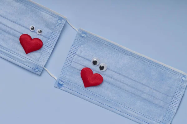 Two medical masks with red hearts on blue background . Love and Coronavirus concept .