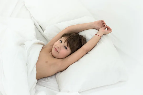 Criança adormecida, o menino está em uma cama em uma roupa de cama branca. Vista superior . — Fotografia de Stock