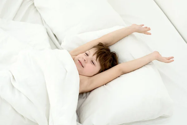 Criança adormecida, o menino está em uma cama em uma roupa de cama branca. Vista superior . — Fotografia de Stock