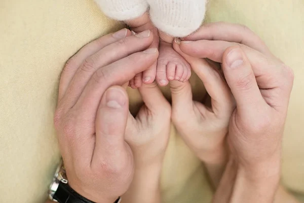 Pieds d'un nouveau-né, orteils dans les mains de maman et papa, les premiers jours de la vie après la naissance, fond jaune, famille — Photo