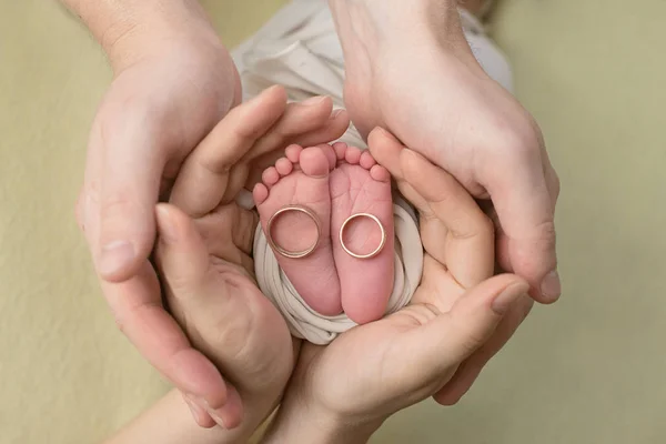 Pieds d'un nouveau-né, orteils dans les mains de maman et papa, les premiers jours de la vie après la naissance, fond jaune, alliances familiales — Photo