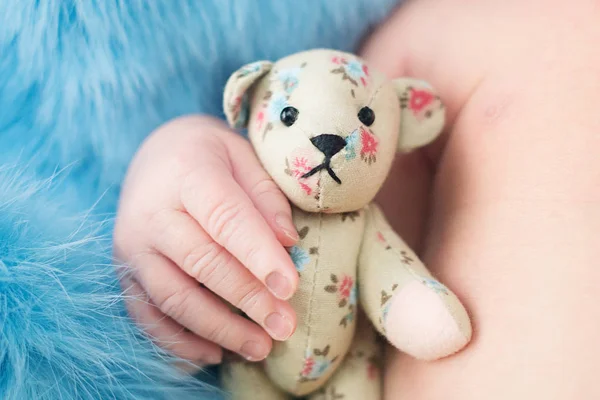 Urso de brinquedo na mão de bebê recém-nascido, mãos e unhas de uma criança, os primeiros dias de vida após o nascimento, pele escamosa — Fotografia de Stock