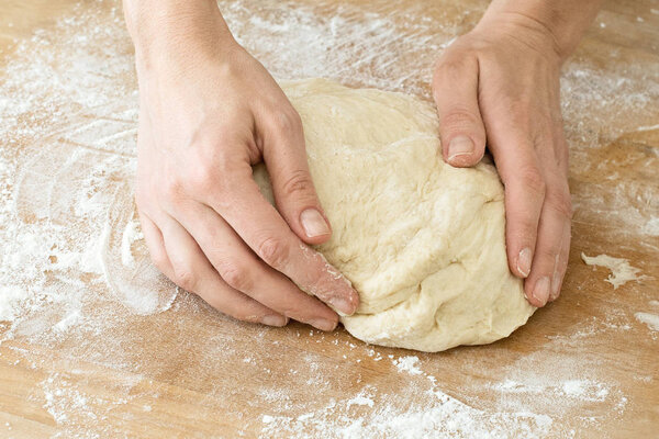 female hands knead the dough on a wooden board cooking baking
