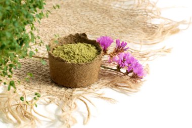 henna powder for dyeing hair and eyebrows and drawing mehendi on hands,  with green  leafs, pink flowers and sackcloth clipart