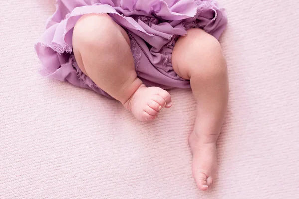 Gambe paffute di una neonata in gonna lilla, giovane ballerina, dita sui piedi, mosse di danza, sfondo rosa, posto per il testo — Foto Stock