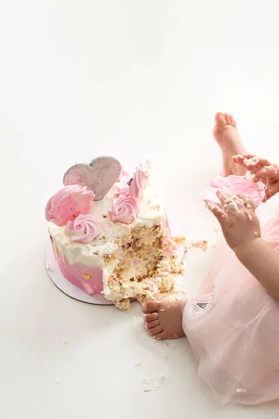 Crash pink cake at the celebration of the first birthday of the girl, ruined sponge cake, broken marshmallow, baby hands and lags. permissiveness, disobedience, eating with hands