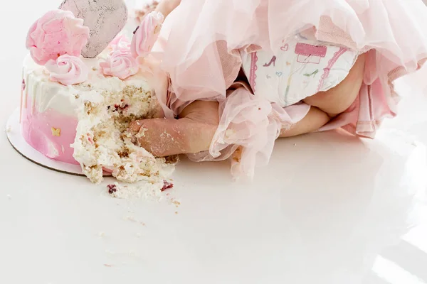 Crash pink cake at the celebration of the first birthday of the girl, ruined sponge cake, broken marshmallow, baby hands and lags. permissiveness, disobedience, eating with hands