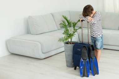 Elinde bavul ve palet olan turist çocuk koronavirüs salgını sırasında evde kalıyor. İzinlerin iptali ve ülkeler arasındaki sınırların kapatılması. Uçuş iptali.