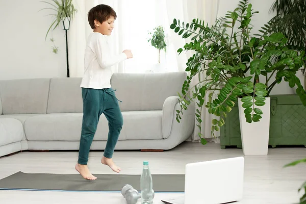 The boy goes in for sports at home online. The child does exercises in the room