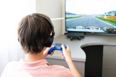 Genç çocuk internet üzerinden kulaklık, joystick ve oyun konsoluyla bilgisayar oyunu oynuyor..