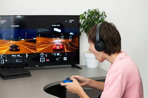 Orenburg, Rusia, 19 de junio de 2020.. Gran truismo deportivo. Adolescente juega un juego de ordenador con auriculares y un joystick, consola de juegos . — Foto de Stock