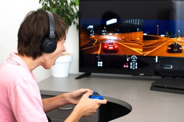 Genç çocuk internet üzerinden kulaklık, joystick ve oyun konsoluyla bilgisayar oyunu oynuyor..