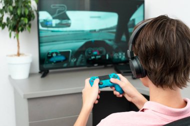 Genç çocuk internet üzerinden kulaklık, joystick ve oyun konsoluyla bilgisayar oyunu oynuyor..