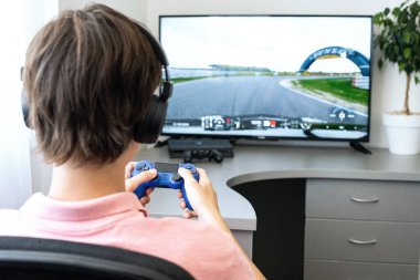 Genç çocuk internet üzerinden kulaklık, joystick ve oyun konsoluyla bilgisayar oyunu oynuyor..