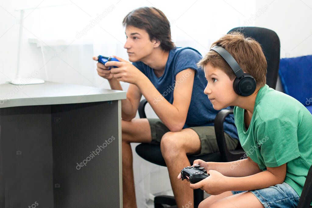 Teenager boy online plays a computer game with headphones and a joystick, game console.