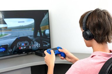 Genç çocuk internet üzerinden kulaklık, joystick ve oyun konsoluyla bilgisayar oyunu oynuyor..