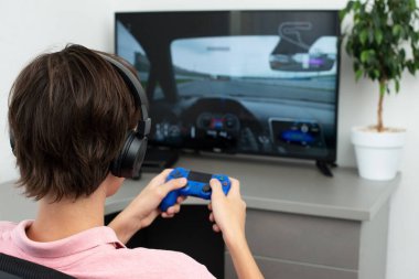 Genç çocuk internet üzerinden kulaklık, joystick ve oyun konsoluyla bilgisayar oyunu oynuyor..