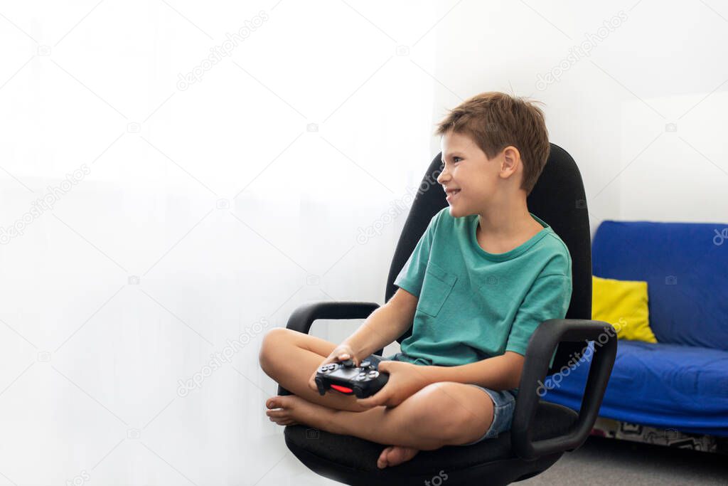 Teenager boy online plays a computer game with headphones and a joystick, game console.