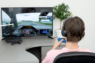 Genç çocuk internet üzerinden kulaklık, joystick ve oyun konsoluyla bilgisayar oyunu oynuyor..