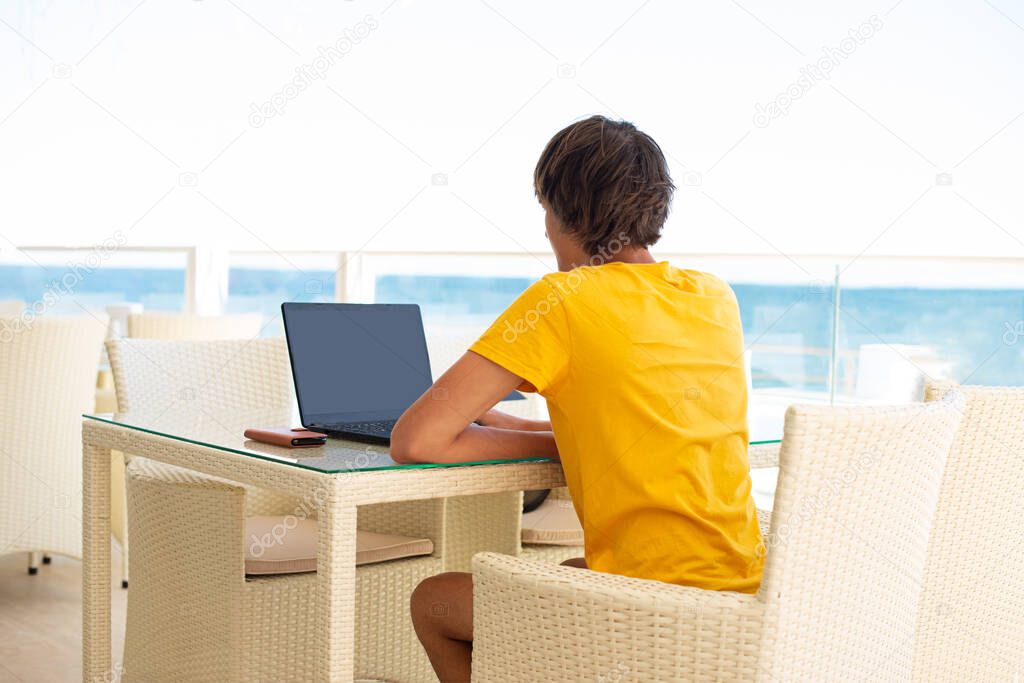 Workplace in a cafe with a sea view. Man working on a laptop in a cafe. Copy space. Mock up.