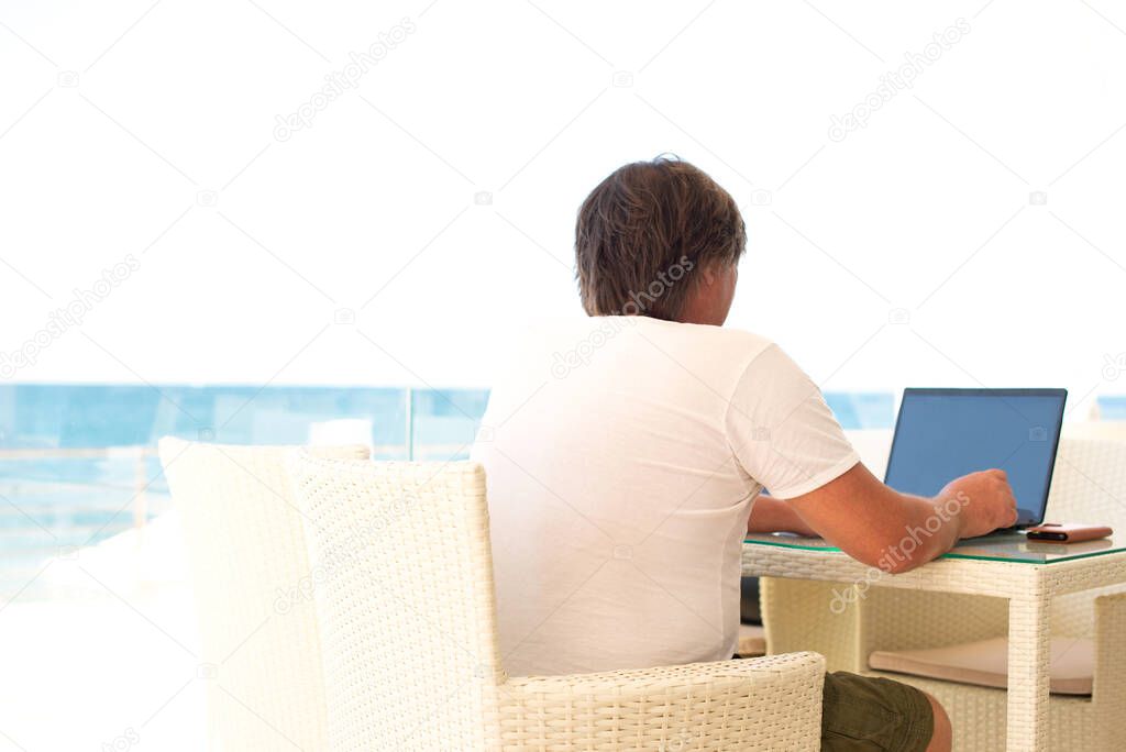 Workplace in a cafe with a sea view. Man working on a laptop in a cafe. Copy space, Mock up. people from behind