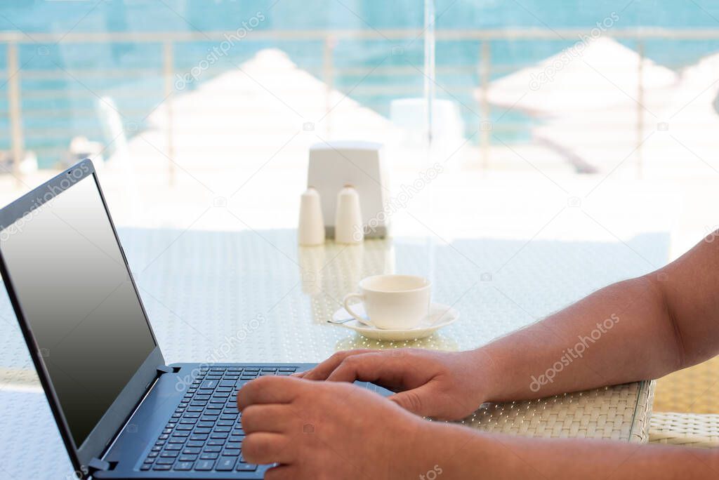 Workplace in a cafe with a sea view. Man working on a laptop in a cafe. Copy space, Mock up.