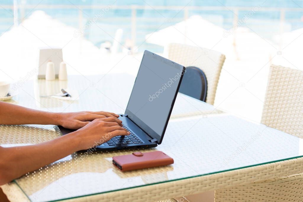 Workplace in a cafe with a sea view. Man working on a laptop in a cafe. Copy space. Mock up.