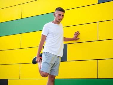 Genç bir beyaz adam kulaklık takıyor ve parlak sarı duvarın yanında çalışıyor.