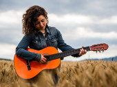 Mělké ostření záběru krásné mladé ženy hrající na kytaru v pšeničném poli