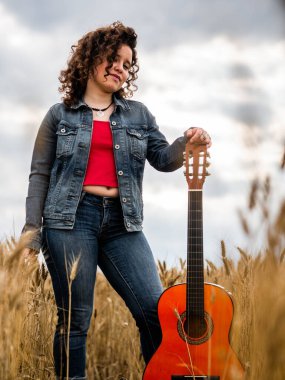 Buğday tarlasında gitar çalan genç ve güzel bir kadının sığ odak noktası.