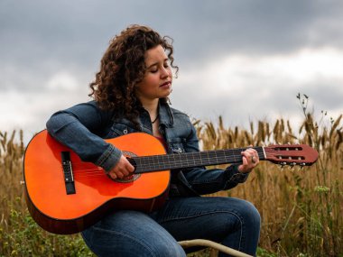 Buğday tarlasında gitar çalan genç ve güzel bir kadının sığ odak noktası.