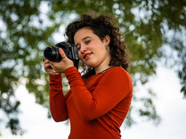 A curly Caucasian woman holding a camera during an outdoors shooting