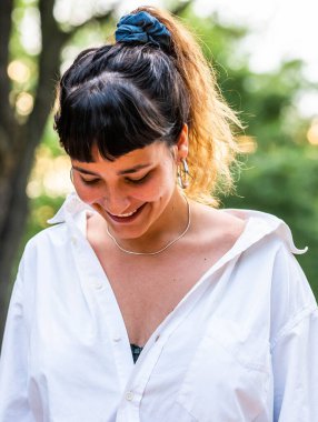 Beyaz gömlekli, harika bir gülümsemesi olan esmer bir kadının dikey resmi.