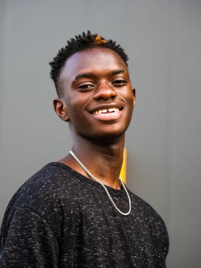 Gri duvar arkasında genç siyah bir erkeğin portresi.