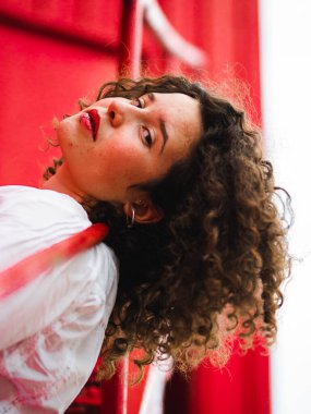 Kızıl arka planda kıvırcık saçlı, beyaz bir kadının sığ odak noktası.