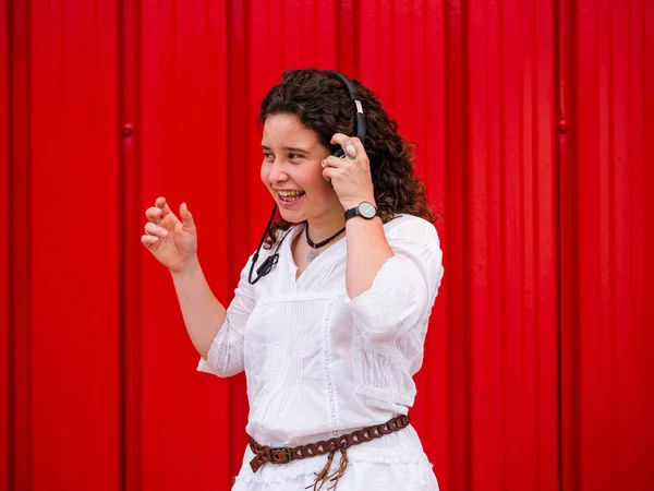 Молода Кавказька Жінка Радістю Слухає Розмови Навушниками Біля Червоної Стіни — стокове фото