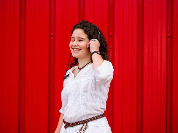 Молода Кавказька Жінка Радістю Слухає Розмови Навушниками Біля Червоної Стіни — стокове фото