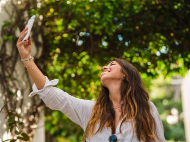  Güzel, çekici bir bayan akıllı telefonuyla selfie çekiyor. Ağaçlarla çevrili bir sokakta selfie çeken bir turist. Sahilde selfie çeken kadın.