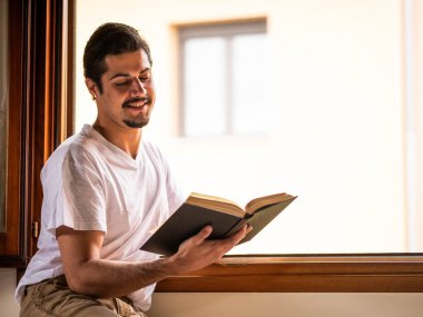 Adam evde oturup kitap okuyor.