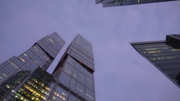 Low angle shot of camera rotating in front of futuristic skyscrapers. Evening — Stock Video