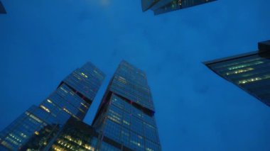 Timelaps. Camdan yapılmış olağandışı şeklin modern gökdelenler. Alt görünüm. Günbatımı